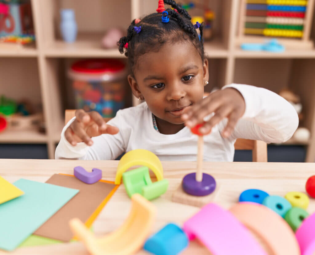 African American girl playing with hoops game sitting on table at kindergarten